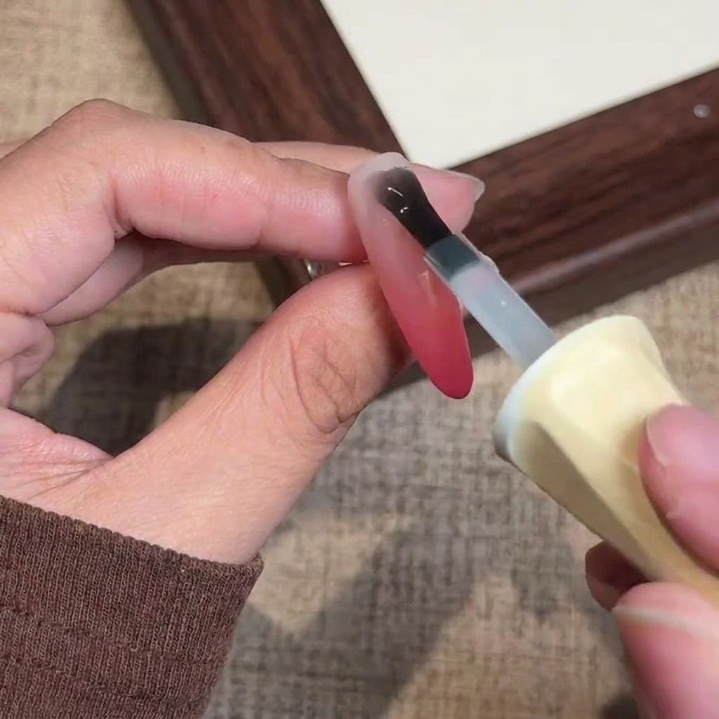Un pincel aplicando la capa final de top coat en gel mate transparente sobre la uña ombré terminada.
