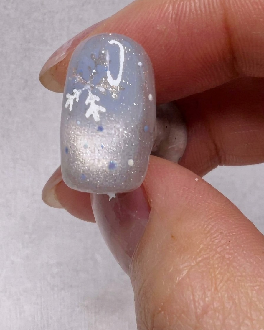 Pincel aplicando una capa de esmalte de gel plateado brillante sobre una uña.