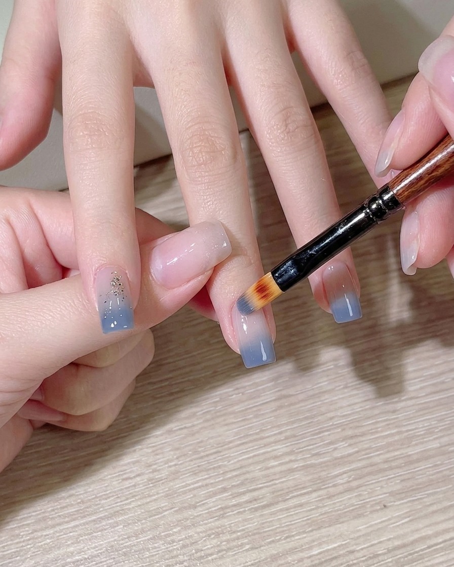 Una esponja de maquillaje aplicando esmalte azul claro sobre una uña.