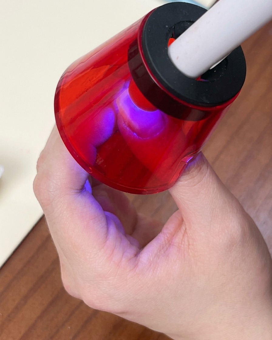 Un pincel aplicando un esmalte en gel ojo de gato blanco brillante sobre la colorida base degradada.