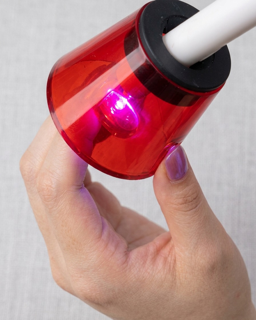 Una uña bajo una lámpara UV/LED roja, curando con las partículas magnéticas de ojo de gato visibles.
