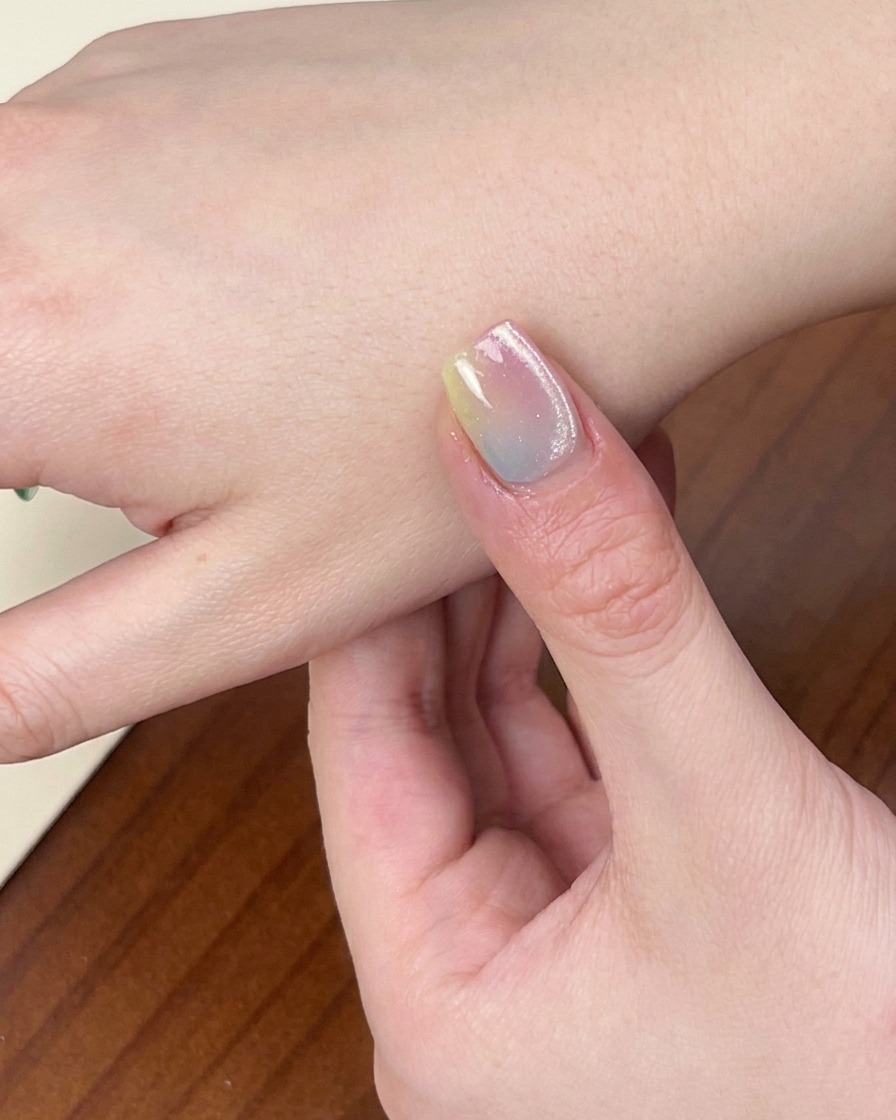Primer plano de una mano con la colorida manicura degradada terminada dentro de una lámpara UV/LED, con la luz encendida.