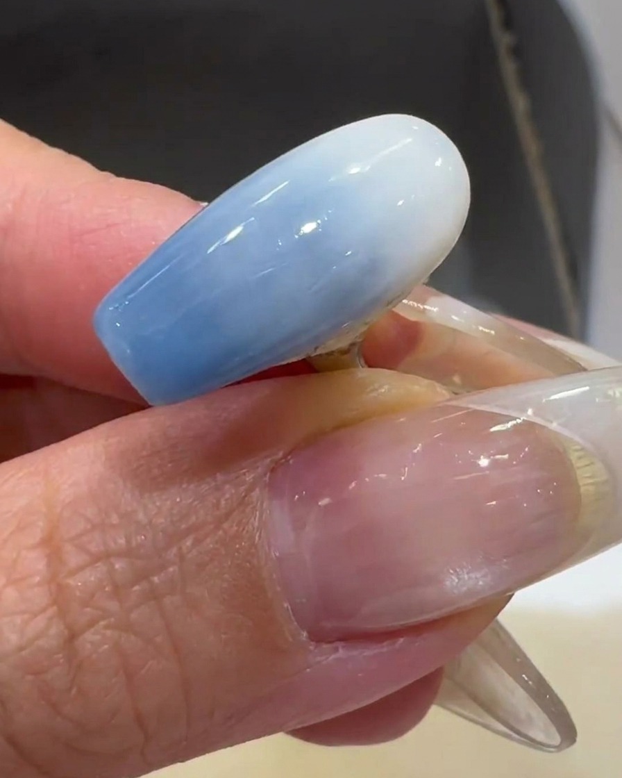 Un pincel aplicando una capa fina de esmalte de gel blanco lechoso sobre un tip transparente.