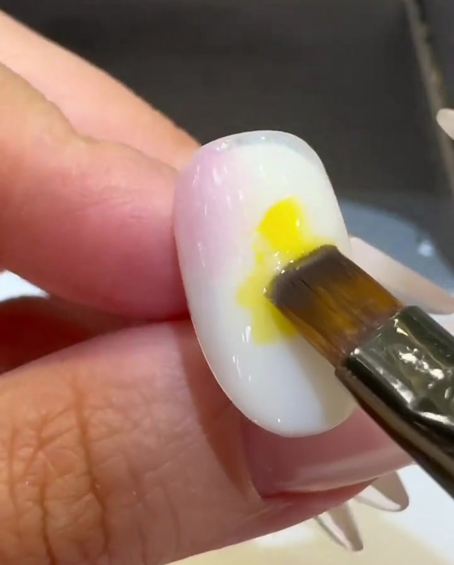 Un pincel plano colocando una gota de esmalte de gel amarillo brillante en el centro de la uña.