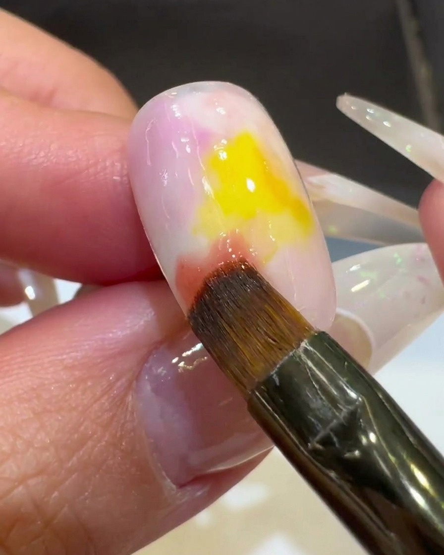 Un primer plano de un pincel mezclando esmalte rosa en el centro amarillo, creando un aspecto degradado.