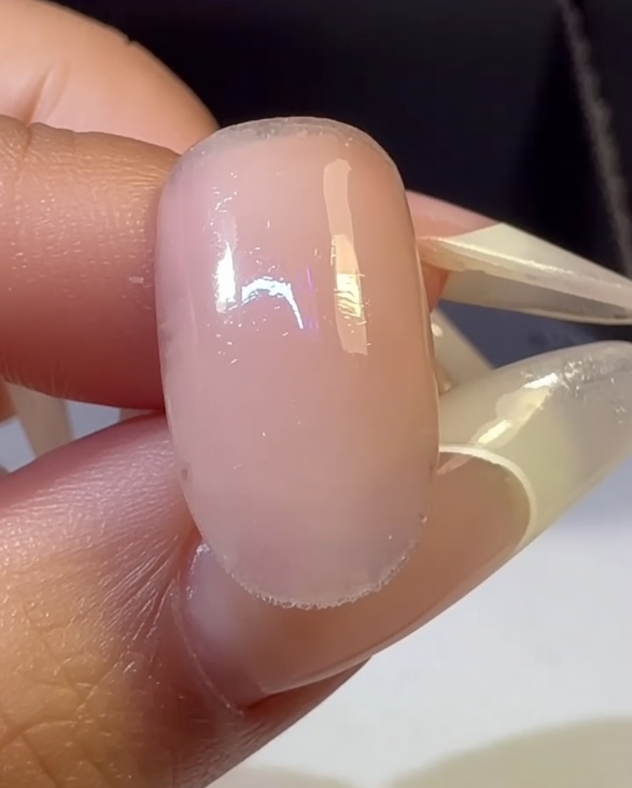 Una mano con una uña de degradado multicolor colocada dentro de una lámpara UV para el proceso de curado.