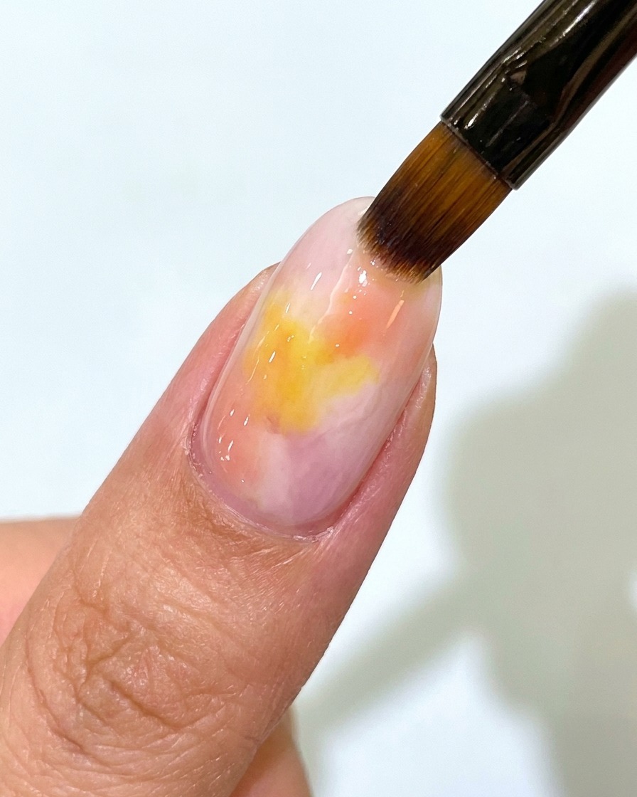 Un pincel aplicando una capa superior mate sobre una uña de gel con degradado rosa y amarillo.