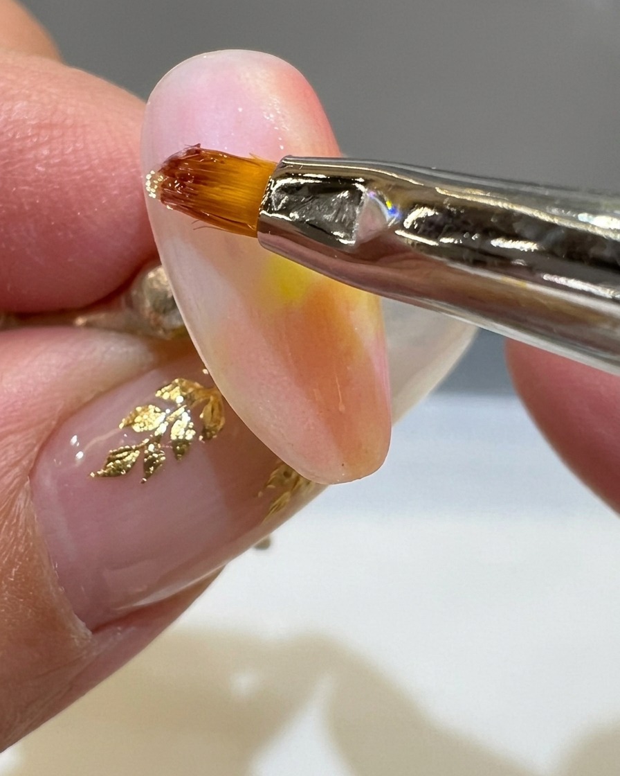 Un pincel delineador fino aplicando una línea gruesa de gel 3D transparente sobre una uña mate color atardecer.