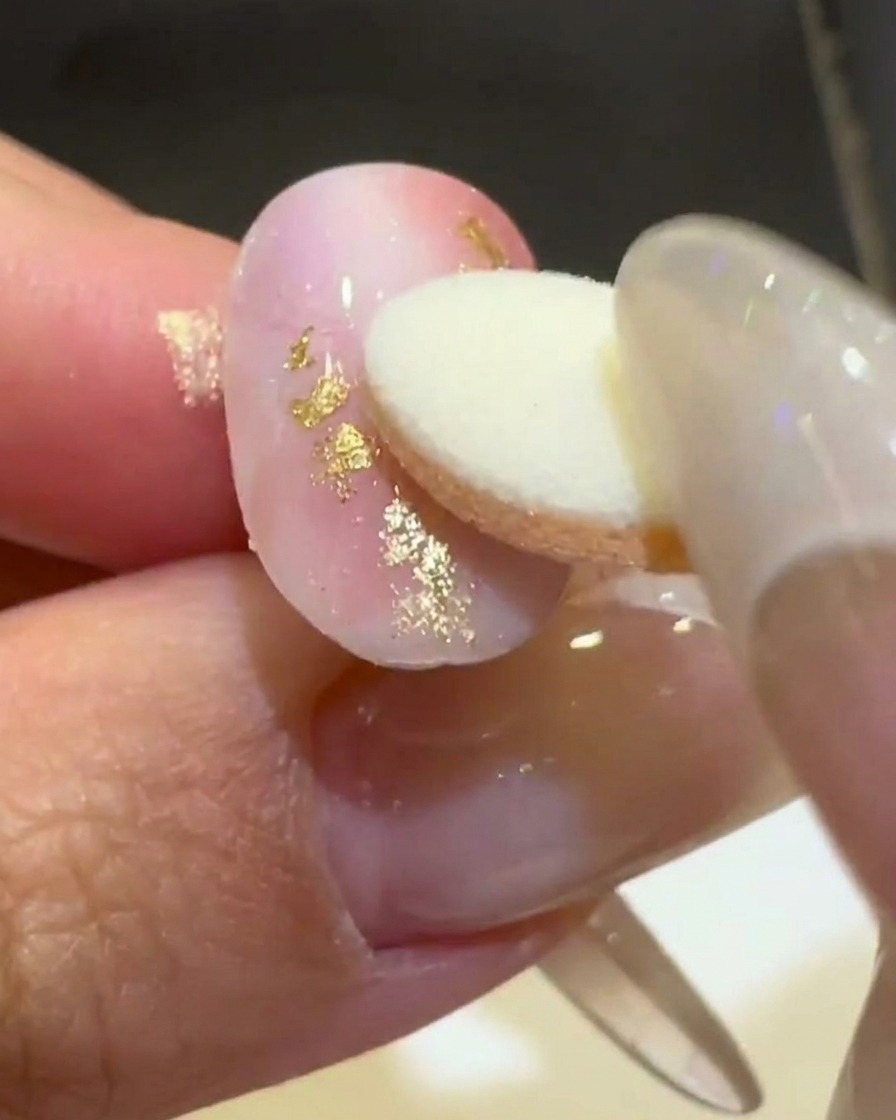 Un aplicador de esponja frotando polvo de cromo aurora dorado sobre una línea ondulada 3D en relieve en una uña rosa y blanca mate.