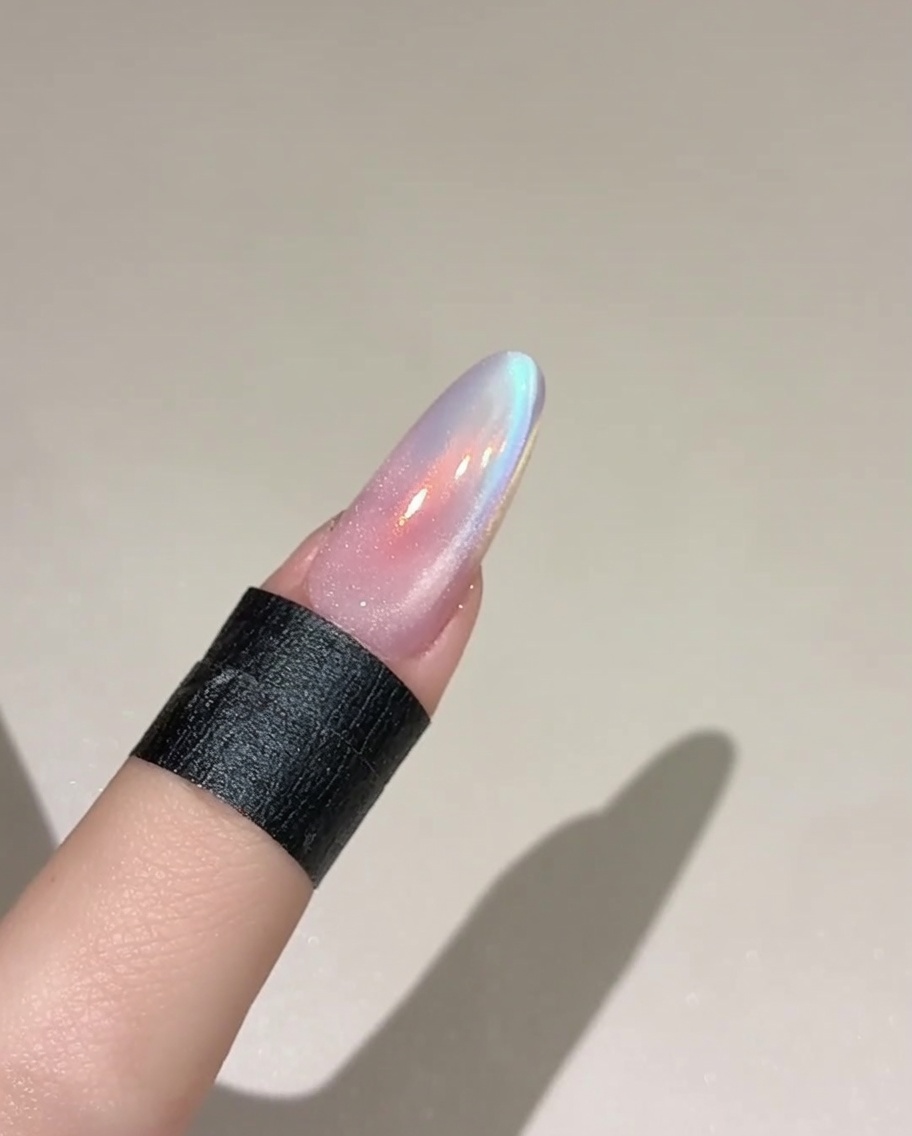 Un pincel aplicando una capa de gel cat eye translúcido y brillante sobre una uña pintada con un color base.