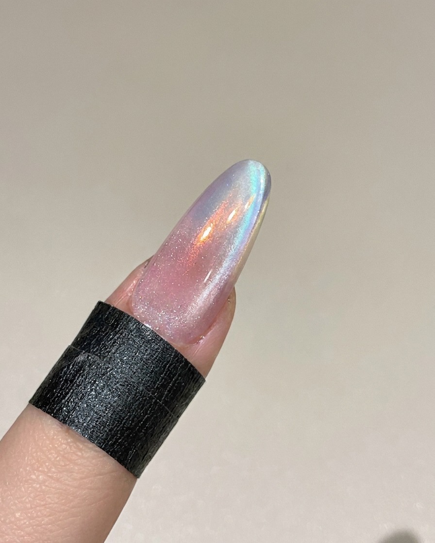 Una herramienta magnética sostenida cerca del lado de una uña para manipular las partículas metálicas en el gel cat eye húmedo.