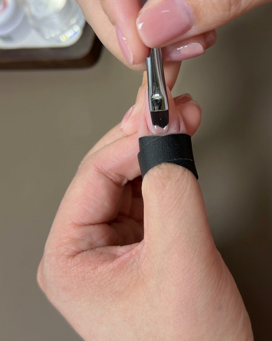 Un pincel aplicando una capa de esmalte en gel nude sobre la uña natural.
