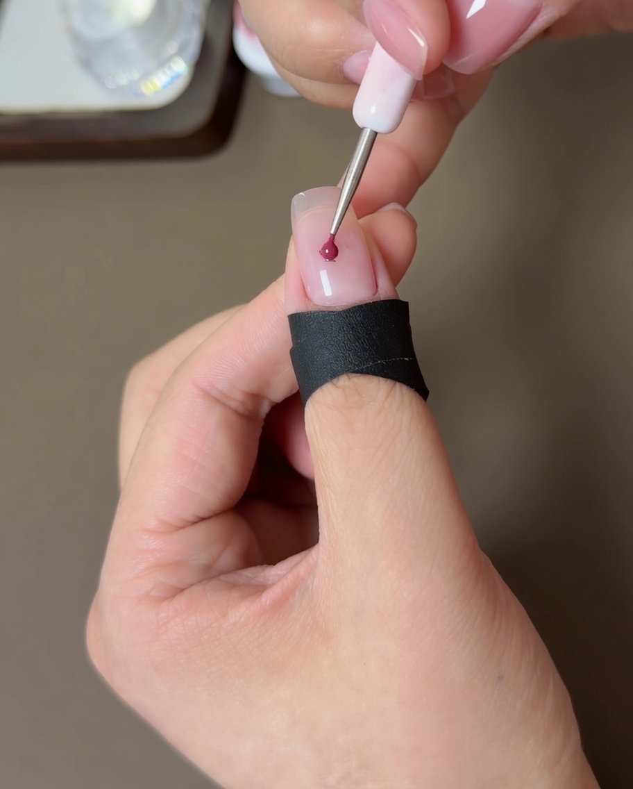 Una herramienta pequeña aplicando una gota de esmalte en gel melocotón en el centro de una uña nude.