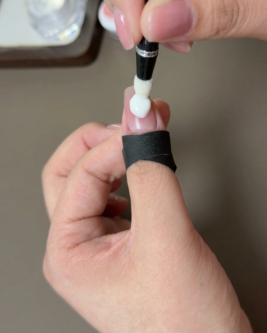 Un primer plano de una mano con la punta de una uña con efecto blush curándose bajo una lámpara UV profesional.