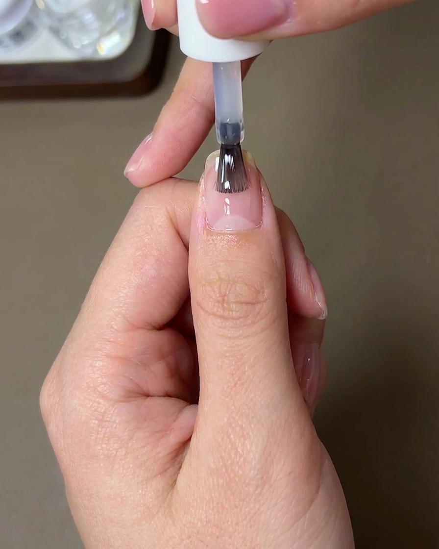 Un pincel aplicando un top coat transparente, brillante y fortalecedor sobre una uña terminada con polvo sunset aurora chrome.