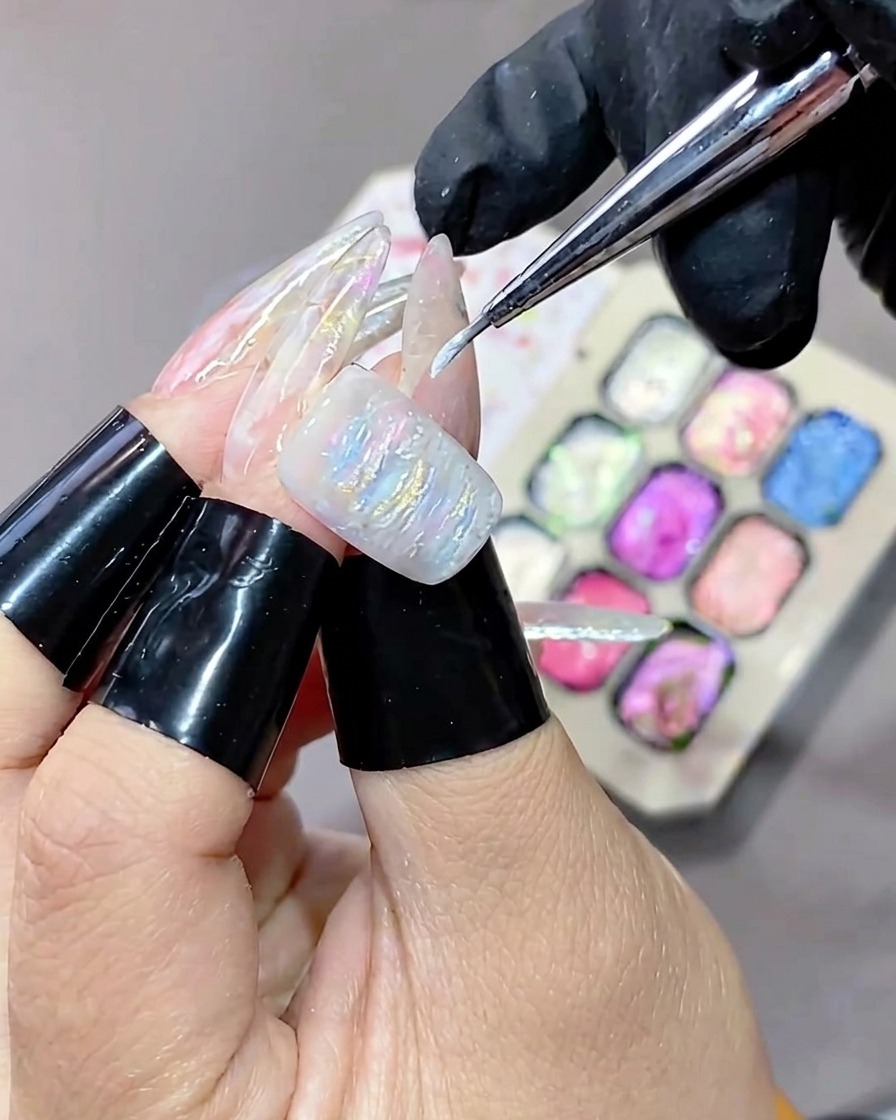 Un pincel de punta fina aplicando gel blanco de iluminación sobre la superficie texturizada de una manicura de gel.