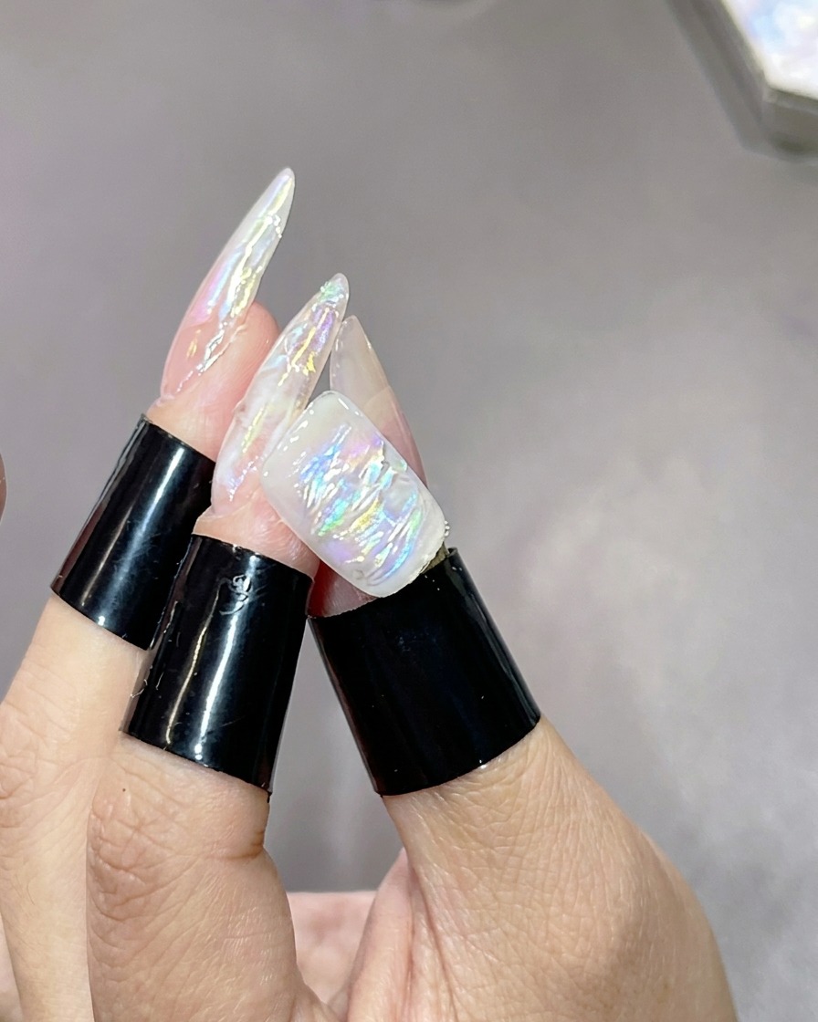 Una mano con uñas jaspeadas y texturizadas descansando dentro de una lámpara de curado UV para fijar la capa de iluminación.