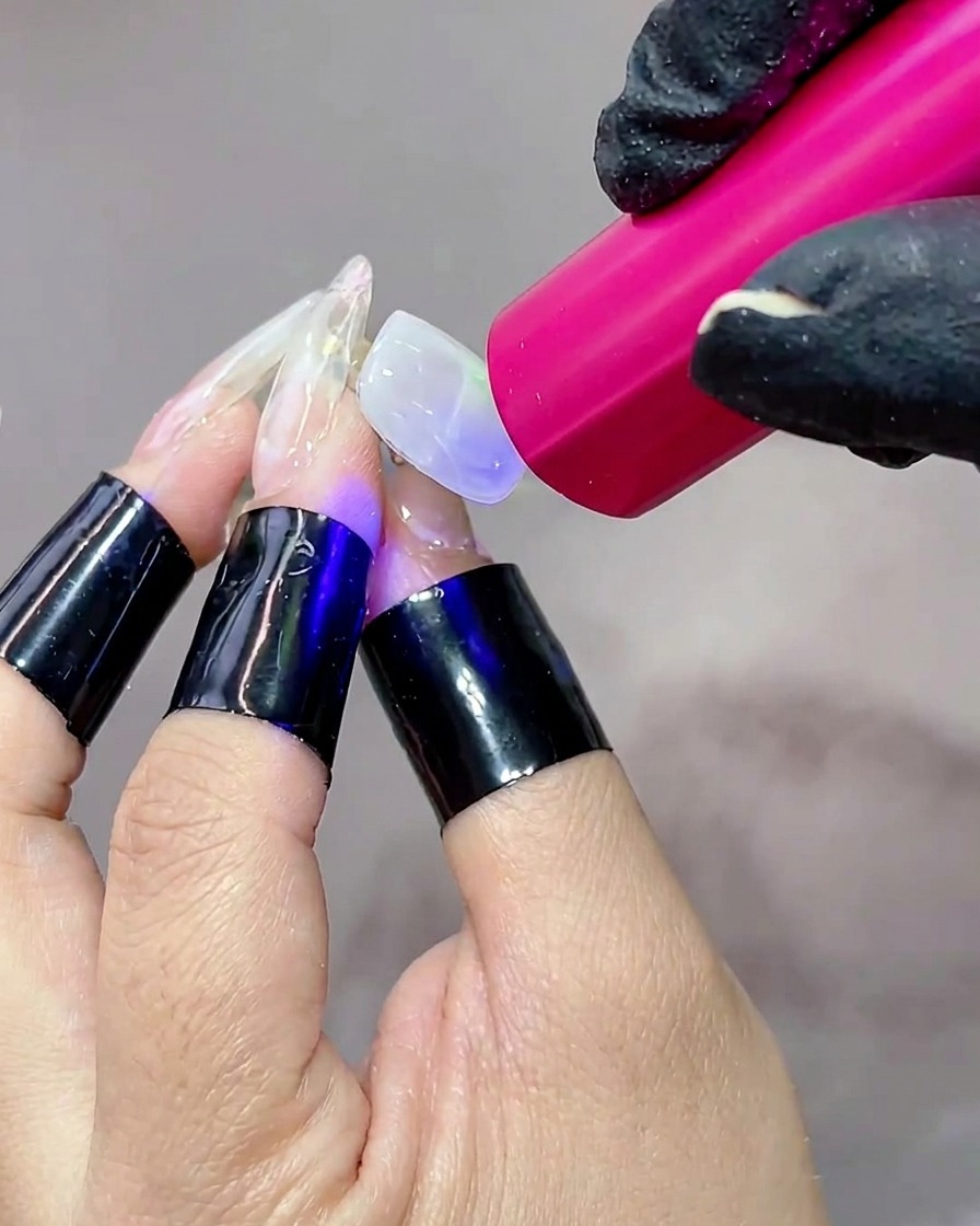 Una mano posicionada bajo una lámpara UV portátil, con la superficie de la uña brillando mientras el gel se cura.