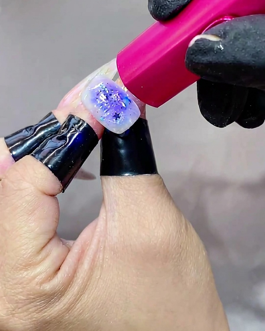 Una mano sosteniendo una uña bajo una lámpara UV brillante, curando la capa final de top coat.