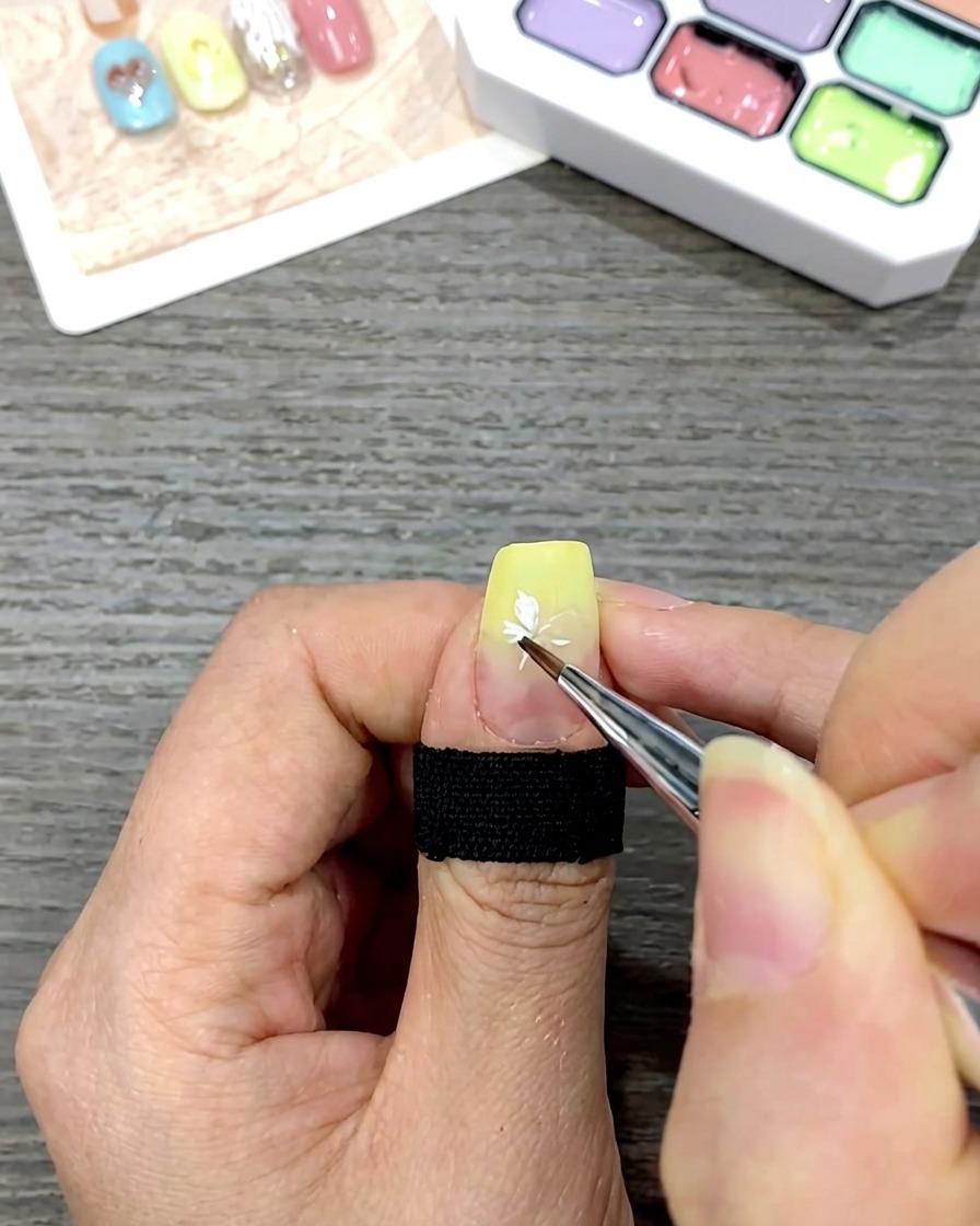 Primer plano de una uña que muestra una flor de margarita blanca completa pintada sobre una base de degradado amarillo.