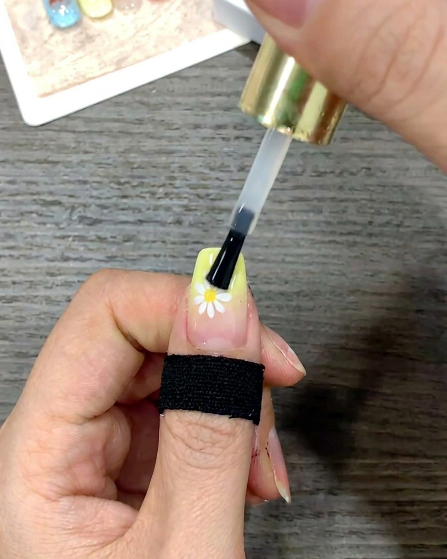 Primer plano de un pincel de uñas suavizando una capa de top coat brillante sobre toda la superficie de la uña.