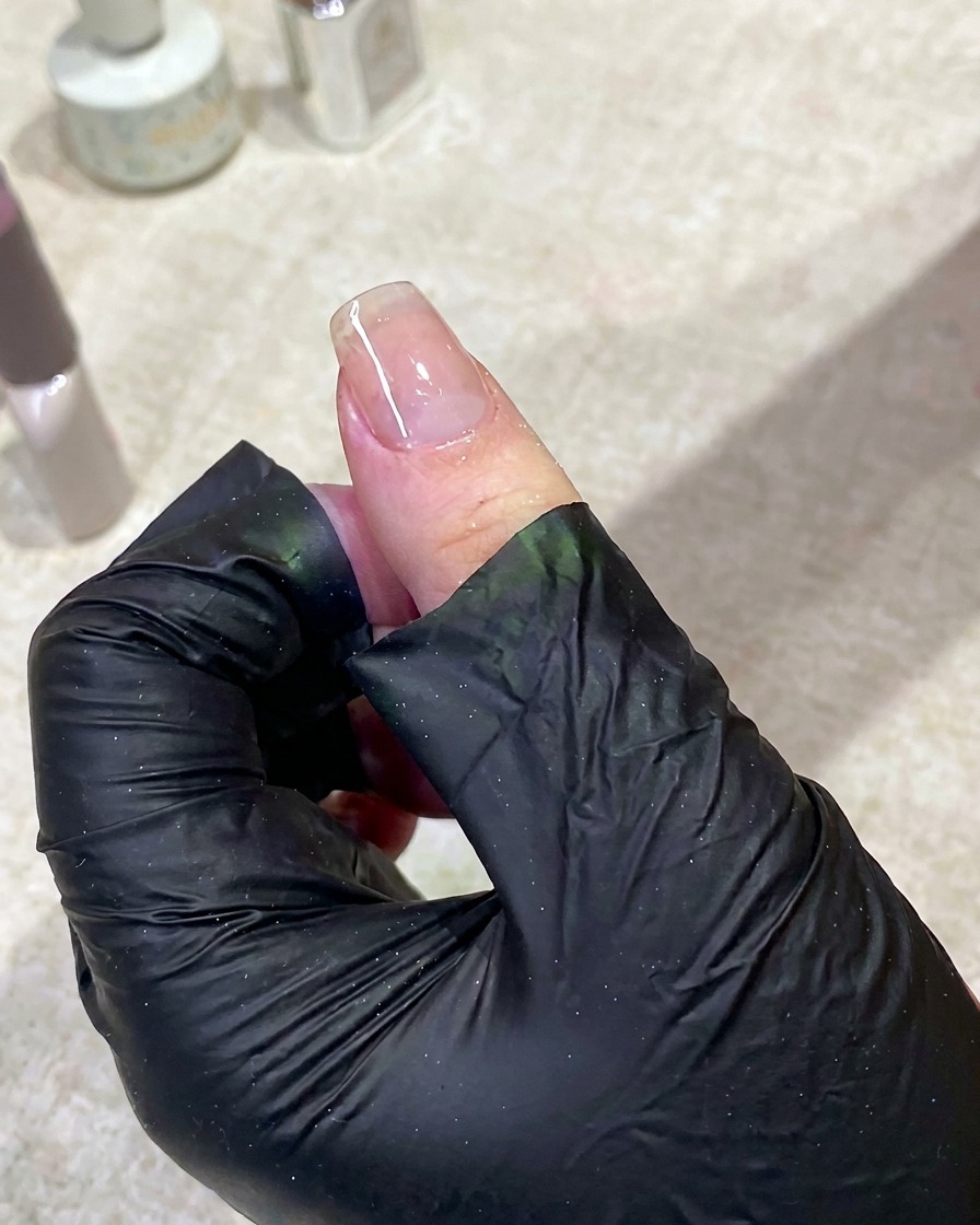 Una mano descansando dentro de una lámpara de uñas UV con la luz encendida, curando la capa base.