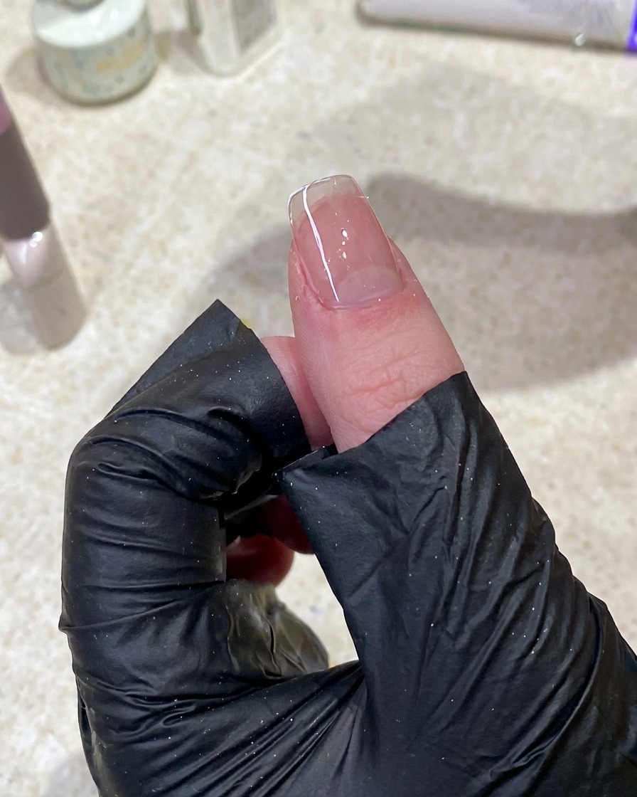 Primer plano de una mano usando una toallita sin pelusa para limpiar la superficie de una uña manicurada.