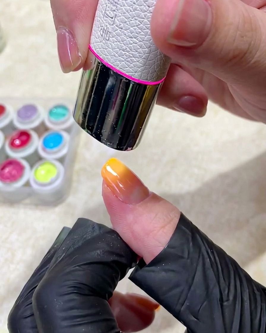 Un dedo manicurado siendo colocado bajo una lámpara de uñas UV profesional para curar la aplicación de esmalte de gel.