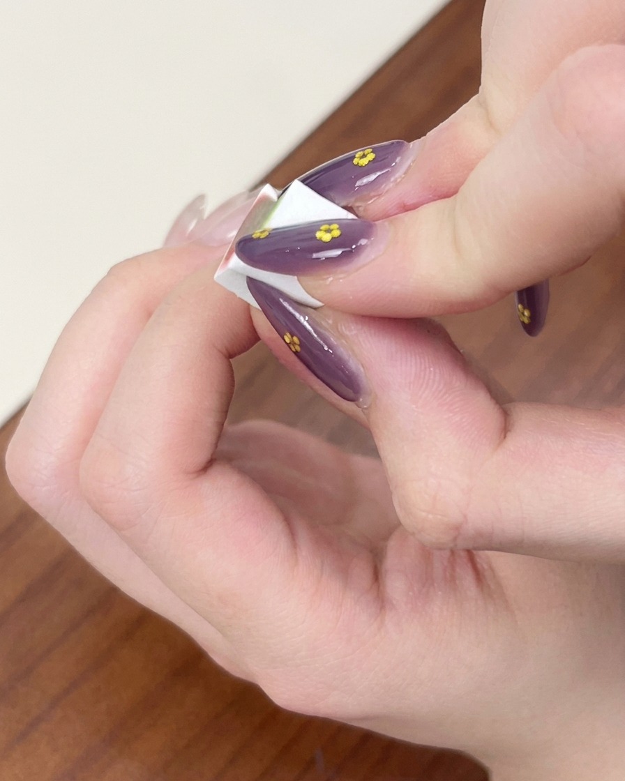 Dedos sosteniendo una pequeña esponja de maquillaje blanca, dando toques para difuminar el gel azul en un efecto ombré sobre una uña.