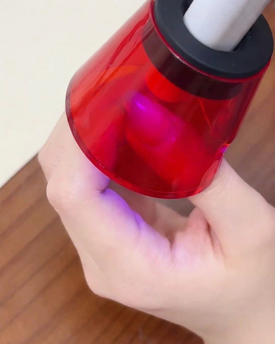 Un dedo descansando bajo una mini lámpara UV portátil roja para curar el esmalte en gel.