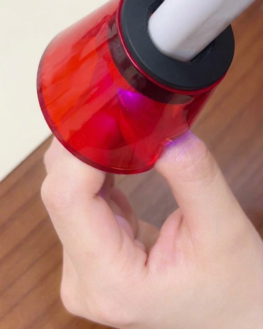 Un primer plano de un dedo colocado bajo una mini lámpara UV/LED roja portátil para el curado final.
