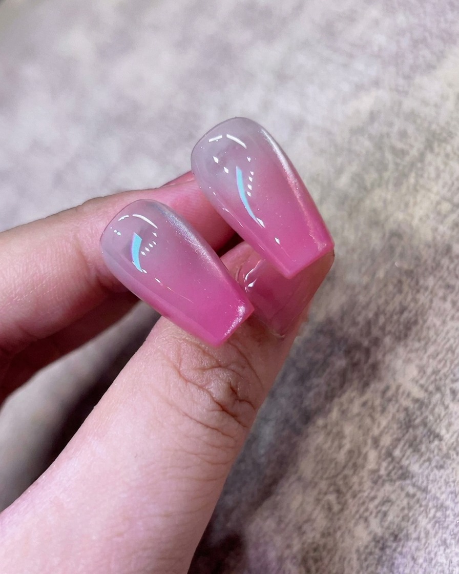 Un pincel aplicando una capa de esmalte en gel cat-eye blanco brillante sobre la uña con degradado rosa.
