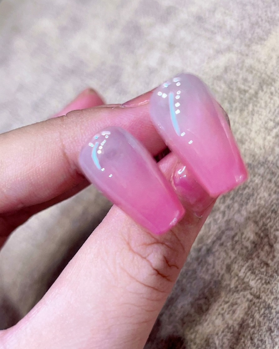 Primer plano de un pincel aplicando un top coat transparente y brillante sobre una uña ombré rosa.