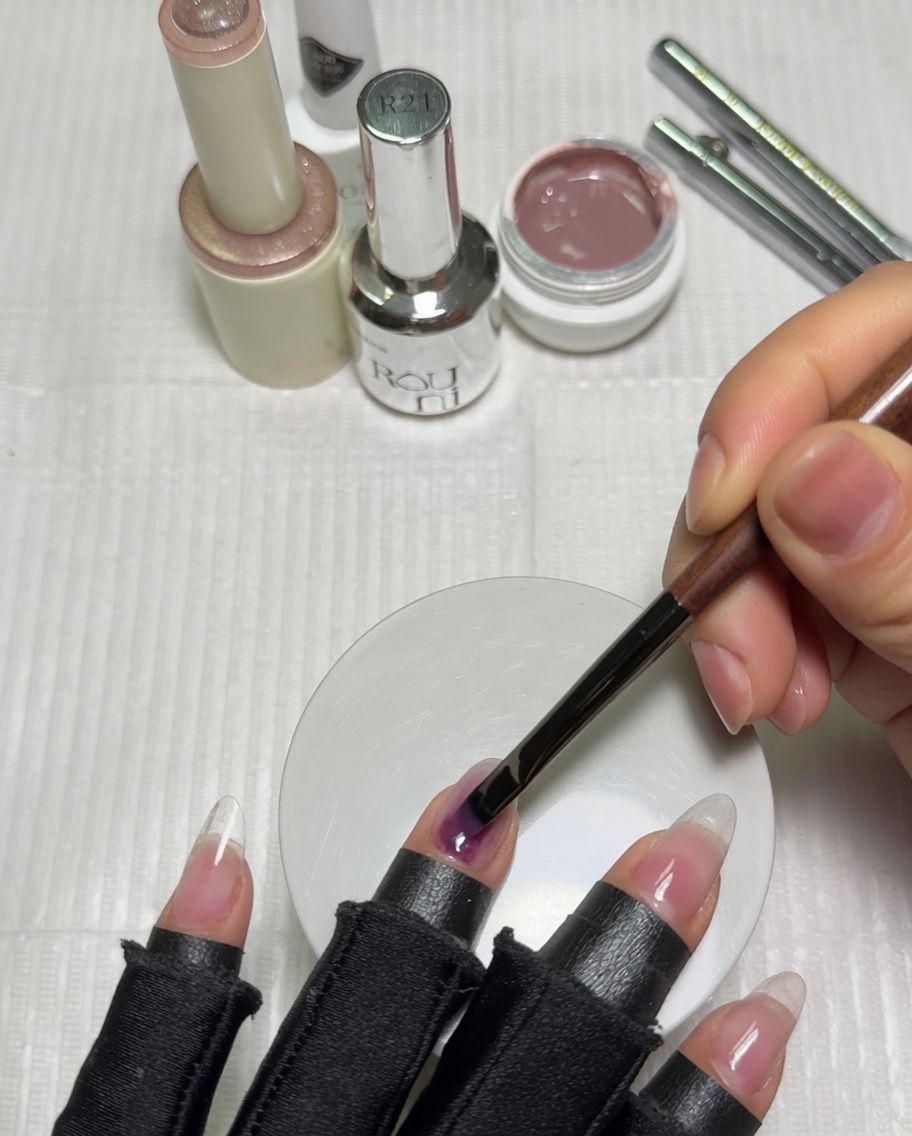 Una mano colocada dentro de una lámpara UV para uñas emitiendo luz violeta, curando la capa base de gel color nude.