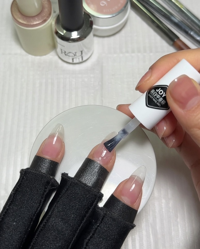 Aplicación de esmalte en gel blanco lechoso en la mitad superior de una uña preparada con base nude rosada usando el pincel del envase.