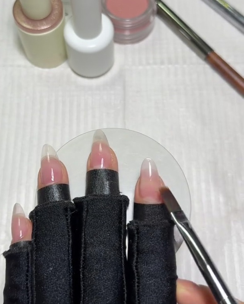 Un pincel plano para degradados barriendo horizontalmente a través de la uña para difuminar el borde del gel blanco lechoso con la base nude.