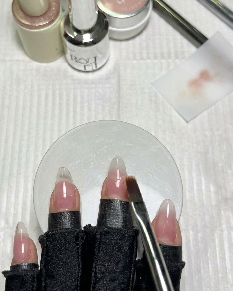 Un pincel plano y limpio difuminando suavemente el borde del esmalte blanco lechoso en la uña adyacente.