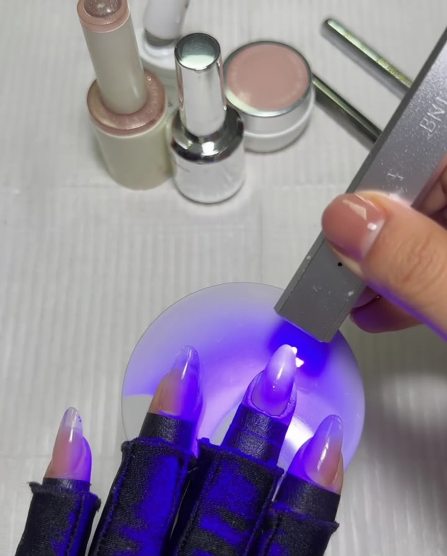Una mano con una manicura degradada colocada dentro de una lámpara UV/LED, curándose bajo la luz violeta.