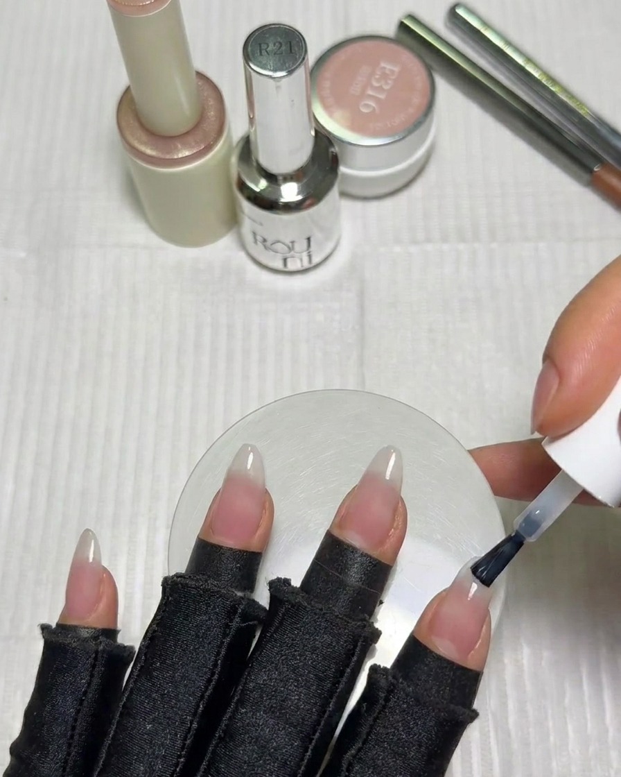 Un pincel de uñas aplicando una pequeña cantidad de gel blanco lechoso en la punta de una uña.