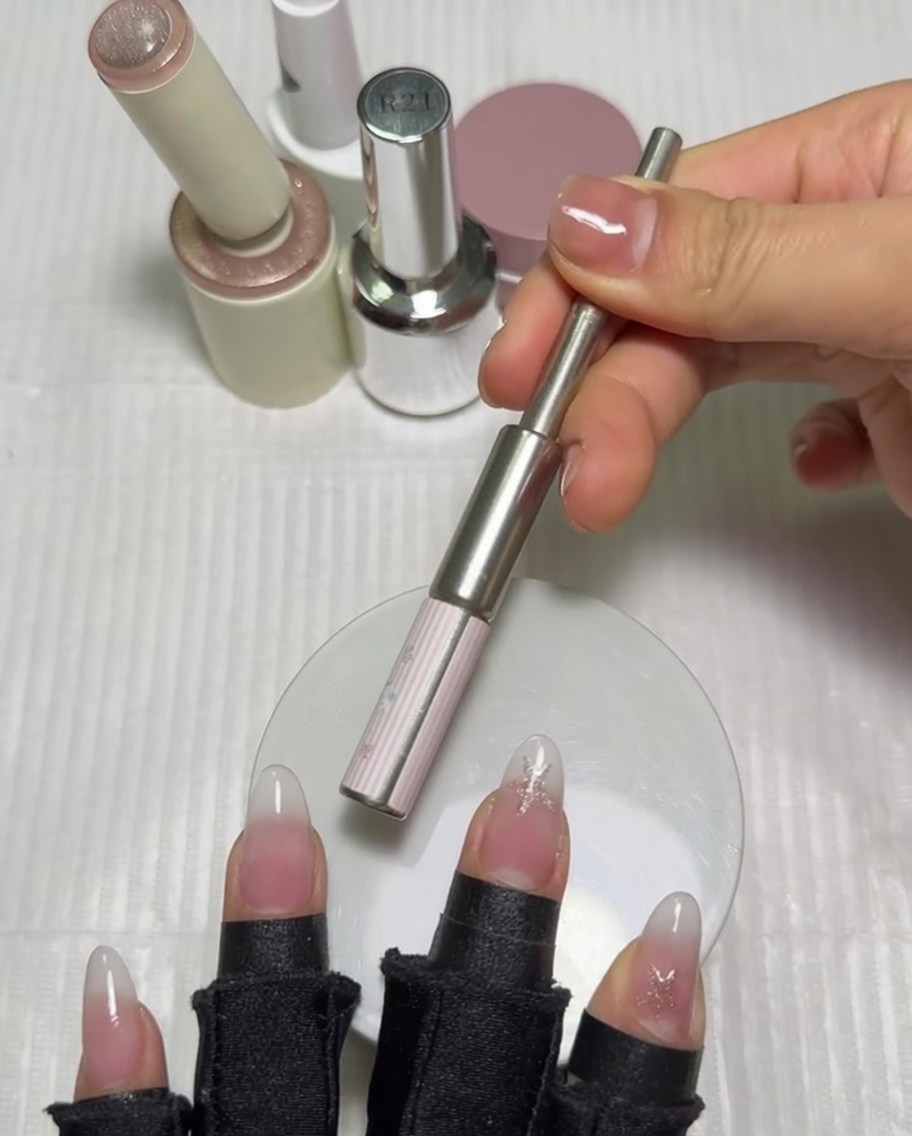 Un imán cilíndrico sostenido horizontalmente sobre la uña del pulgar para activar el esmalte en gel magnético.