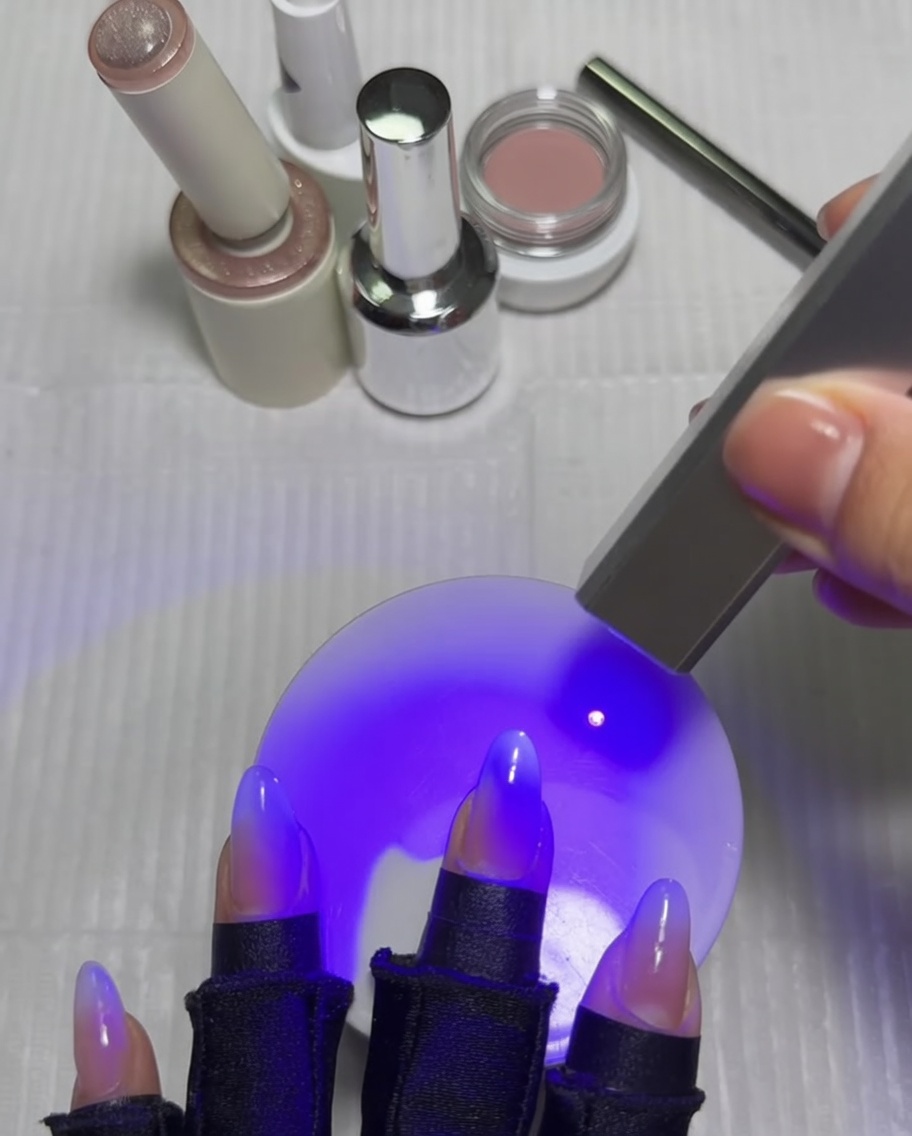 Una mano con las uñas bajo una lámpara UV, curando el pulgar después de terminar el diseño de la estrella ojo de gato.