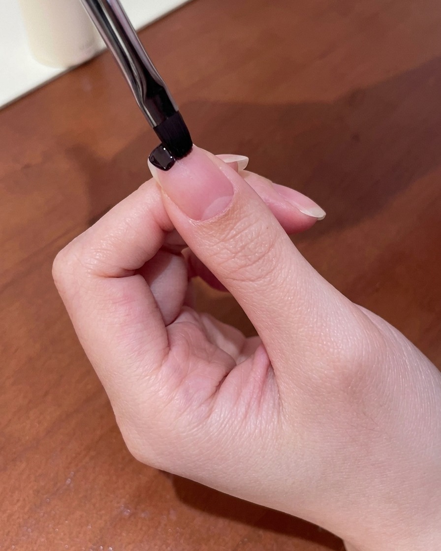 Primer plano de un pincel pequeño aplicando esmalte en gel de color púrpura oscuro en la punta de una uña.