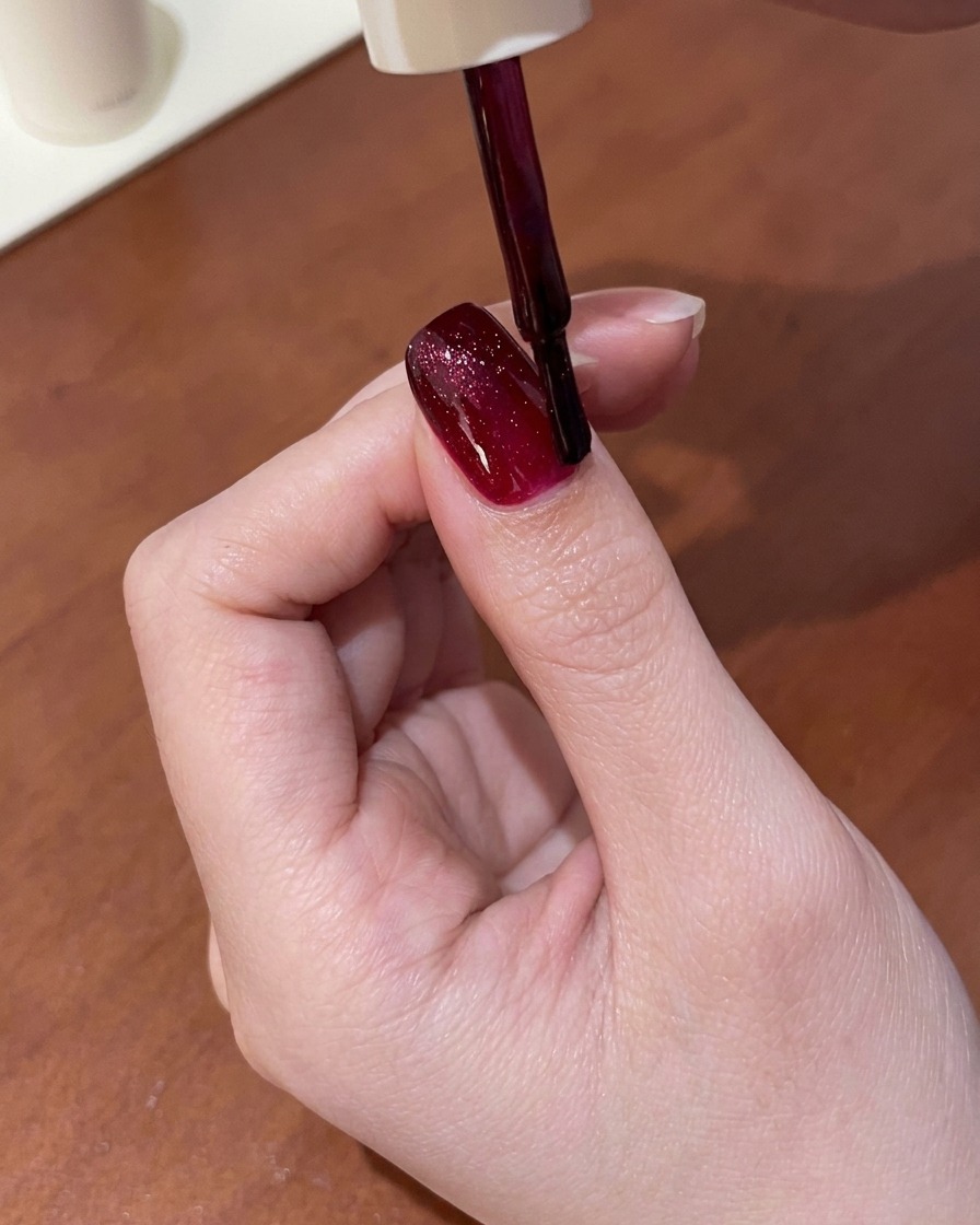Una herramienta magnética sostenida sobre una uña con gel cat-eye rojo húmedo, atrayendo el brillo hacia una línea brillante.