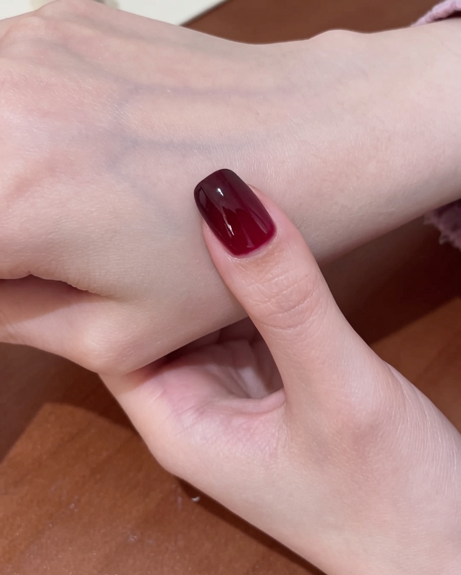 Un pincel aplicando un top coat transparente y brillante sobre el diseño de uñas cat-eye rojo terminado.