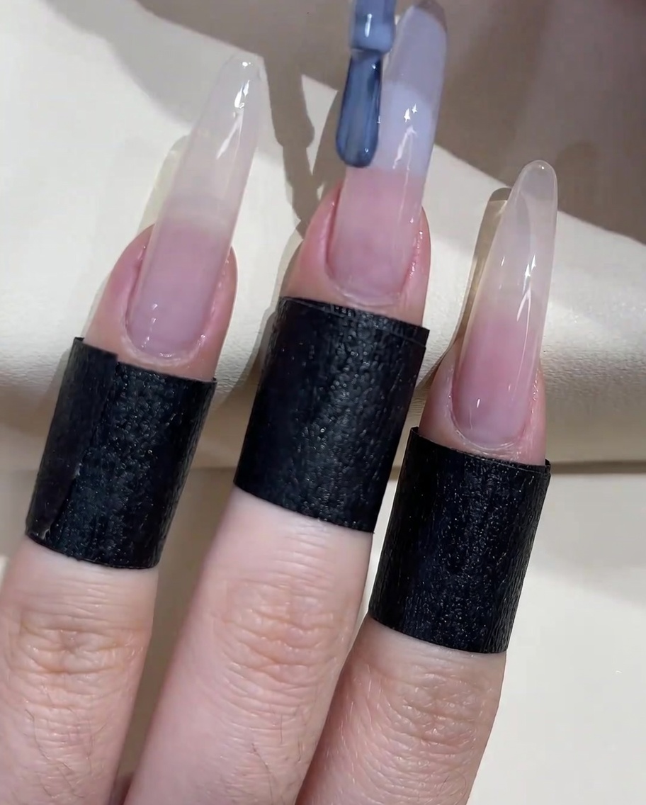 Un pincel de uñas aplicando un esmalte en gel azul grisáceo en el borde libre de la uña.
