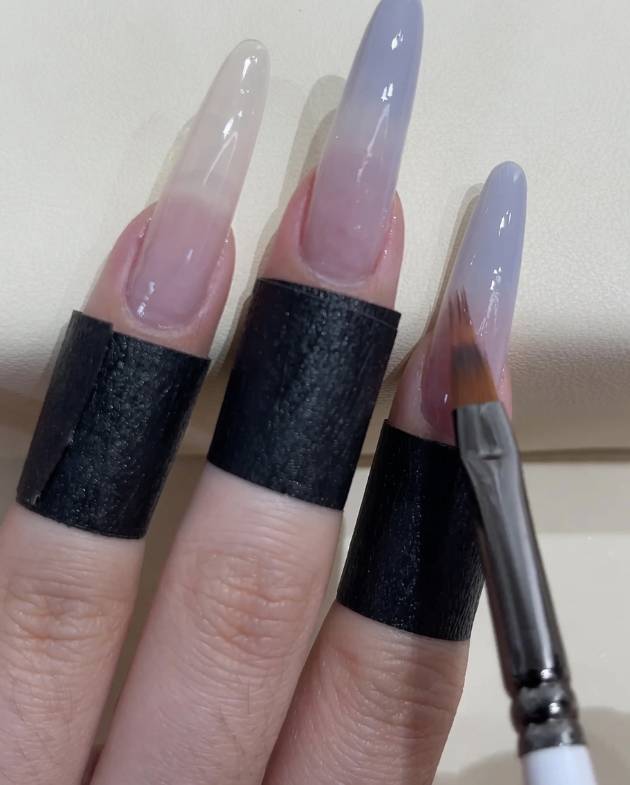 Un pequeño pincel de uñas aplicando más esmalte azul grisáceo en la punta de la uña.