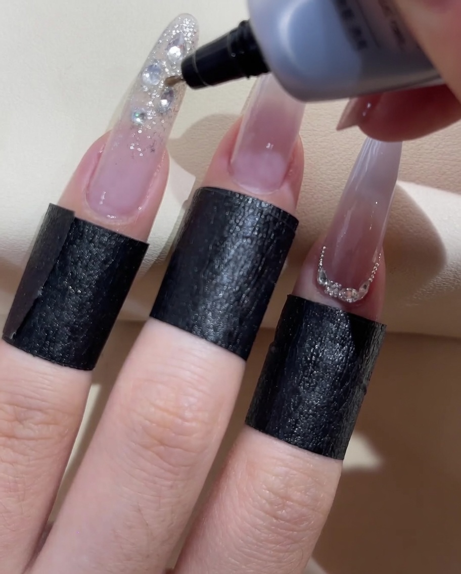 Un frasco de gel de punta fina aplicando gel sellador transparente alrededor de los bordes de la pedrería decorativa.