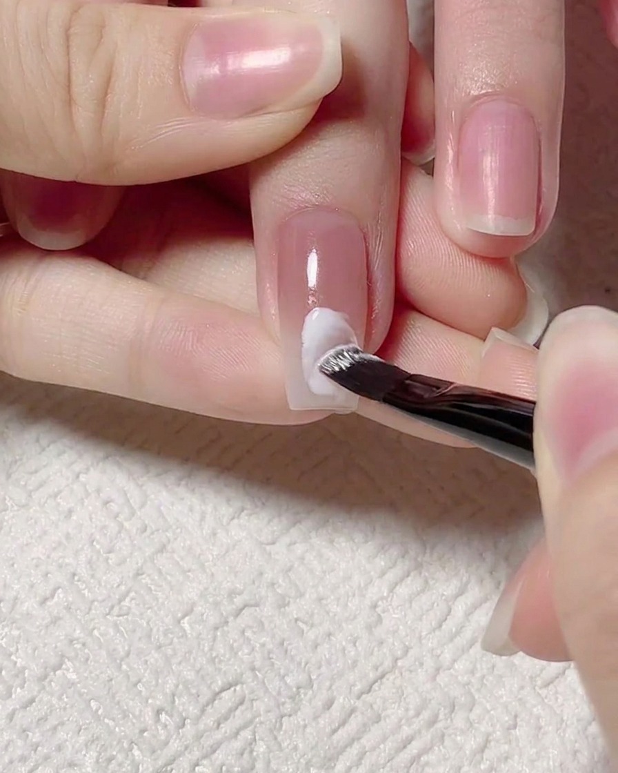 Un pincel de detalle pintando una línea de onda de gel blanco en el centro de la uña.