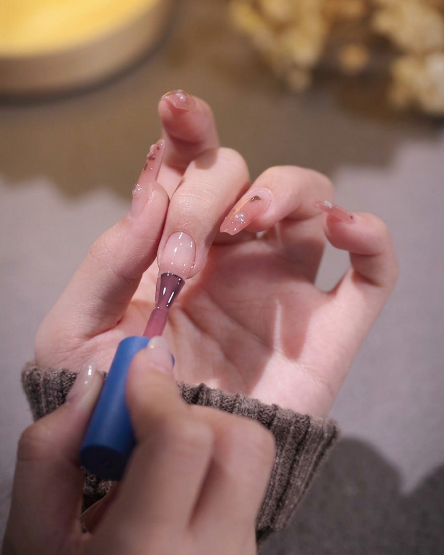 Un pincel de uñas aplicando una capa de esmalte de gel rosa traslúcido sobre una uña preparada.