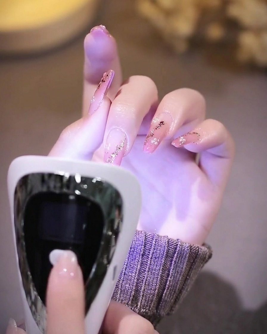 Una mano con uñas terminadas descansando dentro de una lámpara UV mientras el interior brilla con luz púrpura.